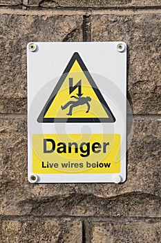 Danger Live Wires Below Warning Sign on a stone brick wall