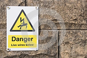 Danger Live Wires Below Warning Sign on a stone brick wall