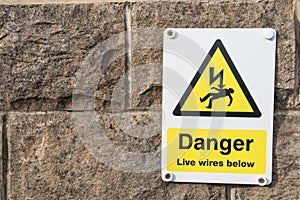 Danger Live Wires Below Warning Sign on a stone brick wall