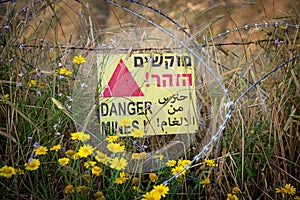 Danger mines -  yellow warning sign next to a mine field, close to the border with Syria, in the Golan Heights, Israel