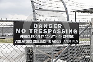 DANGER NO TRESPASSING - VEHICLES ON TRACK AT HIGH SPEEDS VIOLATORS SUBJECT TO ARREST AND FINES sign at a race track