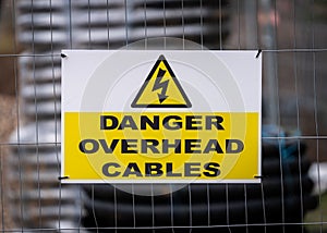 Danger overhead cables modern clean sign in building construction site with yellow electric shock triangle lightening bolt