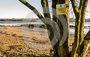 Danger Quicksand, please say clear of the wreck sign on a tree beside a beach