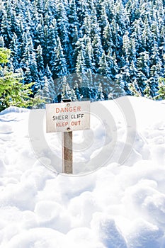 Danger sheer cliff keep off sign on the edge of land cover with snow..