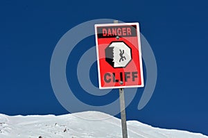 Danger steep cliff sign on snow cape mountain summit