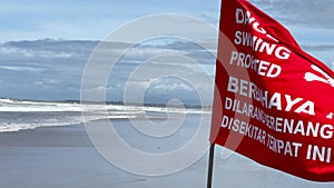Danger, swimming prohibited, red warning flag with a skull on the sandy shore of Bali island in Indonesia. Flag waving