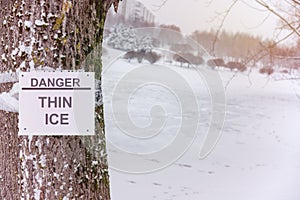 Danger, thin ice inscription on sign attached to tree