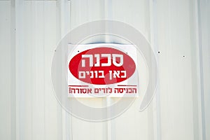 Danger unsafe building in Hebrew sign on a white fence.