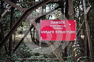 Danger Unsafe Structure sign attached to rusty old metal tower which is in a run down derelict condition keep out risk of injury