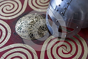Danger, viking helmet with chain mail on a red shield with golden shapes of sun, weapons for war