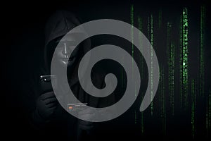 Dangerous anonymous hacker in hooded and mask use smartphone and credit card, break security data and hack password with Bank data