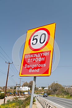 Dangerous bend warning and reduce speed sign. Reduce speed inscription in English and Greek languages