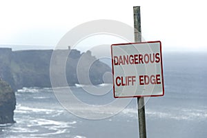 Dangerous cliff edge sign in overcast weather at Cliffs of Moher in Ireland. Danger sign warning.