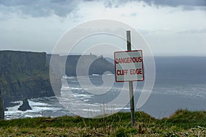 Dangerous cliff edge sign in overcast weather at Cliffs of Moher in Ireland. Danger sign warning.