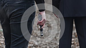 Dangerous criminal man standing behind a man in suit and holding a gun in his hand. Close up