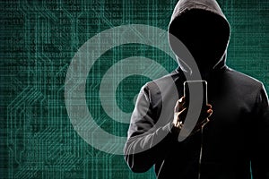 Dangerous hacker with a smartphone gadget over digital background with binary code. Obscured dark face in mask and hood