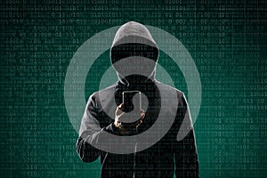 Dangerous hacker with a smartphone gadget over digital background with binary code. Obscured dark face in mask and hood
