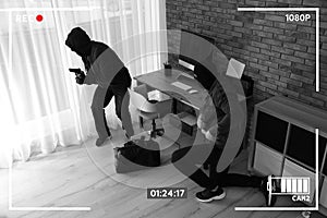 Dangerous masked criminals with weapon stealing money, view through CCTV camera