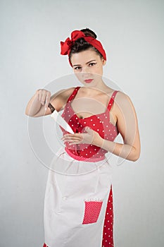 Dangerous pin up girl housewife in red vintage polka dot dress stands with a huge kitchen knife in her hands and angrily rejoices