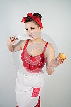 Dangerous pin up girl housewife in red vintage polka dot dress stands with a huge kitchen knife in her hands and angrily rejoices