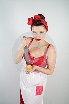 Dangerous pin up girl housewife in red vintage polka dot dress stands with a huge kitchen knife in her hands and angrily rejoices