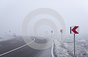 Dangerous road curve and warning signs in a dense mist