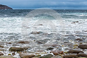 Dangerous sea wave crashes on a rocky coastline with splashes and foam before a storm