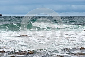 Dangerous sea wave crashes on a rocky coastline with splashes and foam before a storm