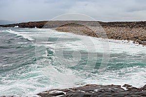 Dangerous sea wave crashes on a rocky coastline with splashes and foam before a storm