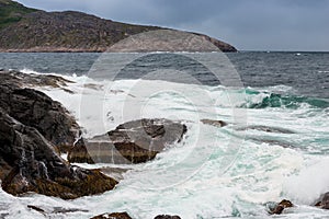 Dangerous sea wave crashes on a rocky coastline with splashes and foam before a storm