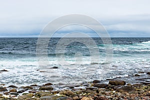 Dangerous sea wave crashes on a rocky coastline with splashes and foam before a storm in the Barents