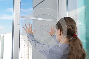 A dangerous situation, a child pushes a mosquito net out of the window, against the sky