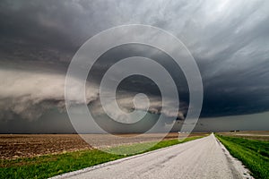 Dangerous storm with shelf cloud approaches quickly over a farm field along a road.