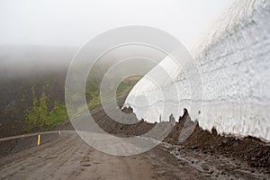 Dangerous wall of snow above the road in Iceland in foggy weather
