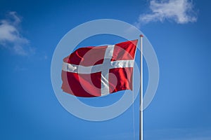 Danish flag in sunshine against blue sky with clouds, horizontal photo