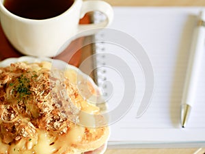 Danish pastry with a cup of hot tea and a pen and small notebook on wood table in morning time