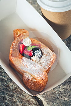 Danish puff pastry with cream and berries in a craft paper box and cup of coffee. Outdoor food eating or Take away food concept