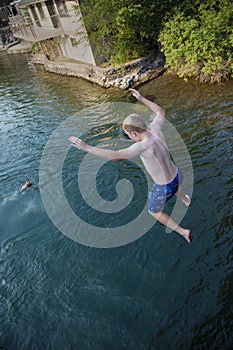 Daring young boy jumping off a bridge into the river. Being adventurous and brave, diving right into the water