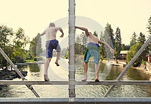 Daring young boys jumping off a bridge into the river. View from behind.