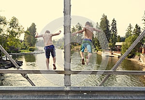 Daring young boys jumping off a bridge into the river. View from behind.