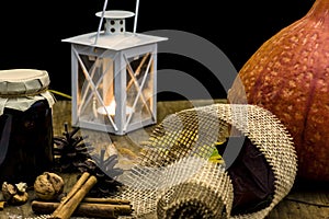 Dark autumn still life with pumpkin, candle and lamp, with yellow leaves of trees on old wooden table board