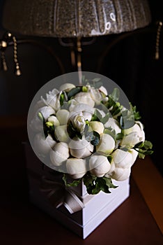 on a dark background is box with white flowers, buds of white peonies are on the table, a thrash in the background