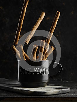 On a dark background, fragrant cinnamon sticks in a black cup. Minimalism. Oriental spices and seasonings. Ingredient for