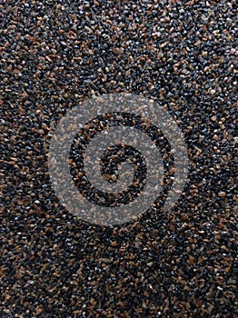 A dark background of many small stones in close-up. Abrasive surface.