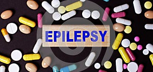 On a dark background, multi-colored pills and the word EPILEPSY on a wooden block. Medical concept