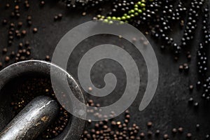 Dark background showing a stone mortar up close and black peppercorns