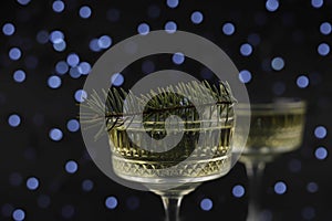 on a dark background there are two transparent figured glasses with champagne, decorated with a Christmas tree branch. holiday