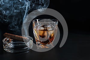 Glass of cold whiskey with cigar on dark background photo