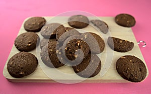 Dark baked chocolate cookies on wooden cutting board on pink acrylic background. Top view. Food photography, dessert, snack, cafe