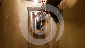 A dark basement, a long corridor with old rusty metal doors and pipes. Illuminated tunnel in a bomb shelter, Cold War underground